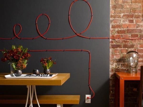 Cables eléctricos rojos instalados en una pared negra.