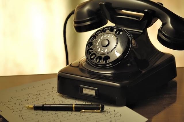 Un viejo teléfono acostado sobre una mesa con un lápiz y una carta