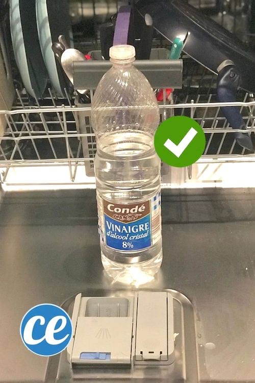 En flaske hvid eddike foran en opvaskemaskine fuld af snavset service