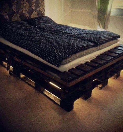 Taaskasutatud puidust alusest vedruga voodi, mille all on valgus