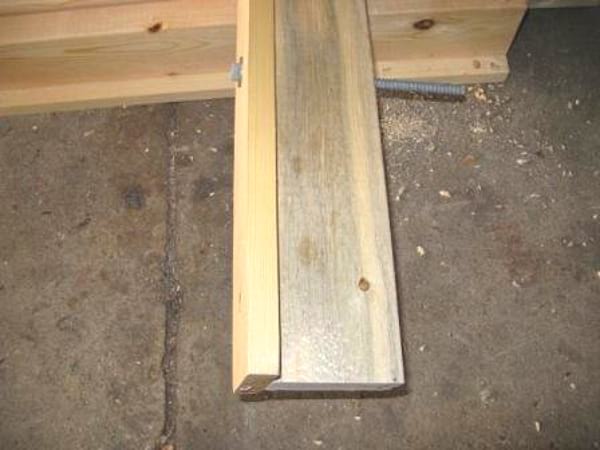 Tirafondo que atraviesa 2 tablones de madera montados en forma de T, sobre suelo de hormigón.
