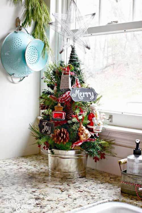 Un pequeño árbol de Navidad decorado y plantado en una maceta frente a la ventana de la cocina.