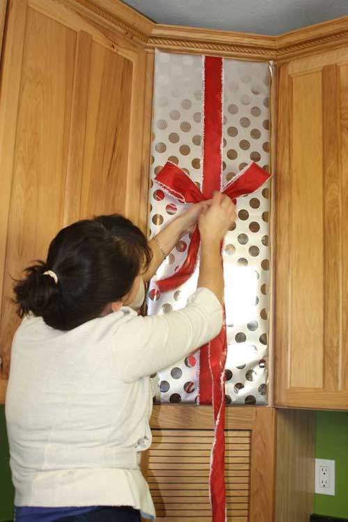 Mujer colgando una cinta roja en la puerta de un armario de cocina como decoración navideña