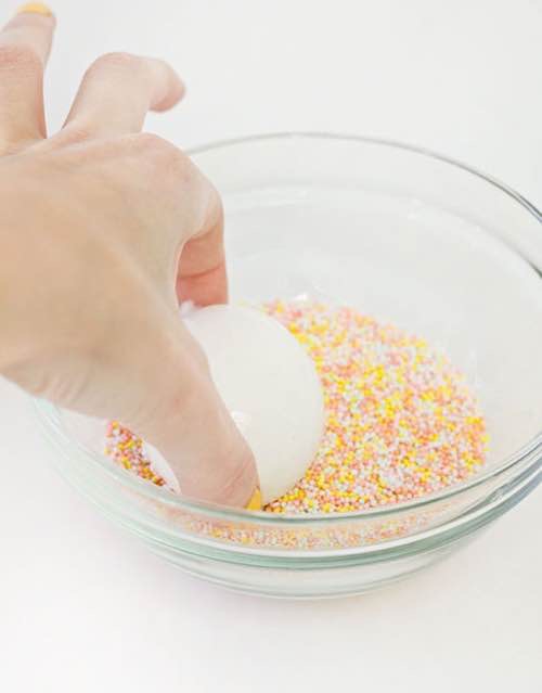 untar el huevo con pegamento y mojarlo en las bolitas de azúcar de colores