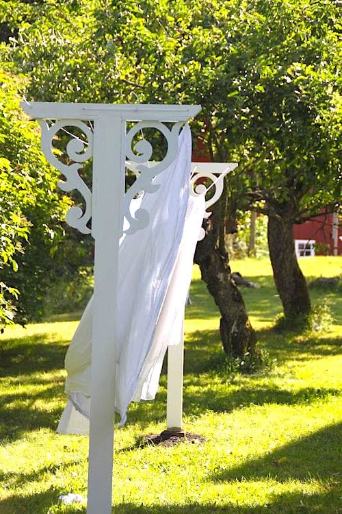 Un estenedor antic pintat de blanc amb fusta tallada en un jardí per assecar els llençols.