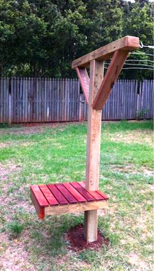 Un poste de madera para tender la ropa con un banco en un jardín.