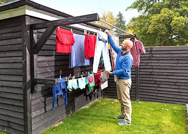 Un hombre secando la ropa en el jardín en un perchero de madera montado en la pared.