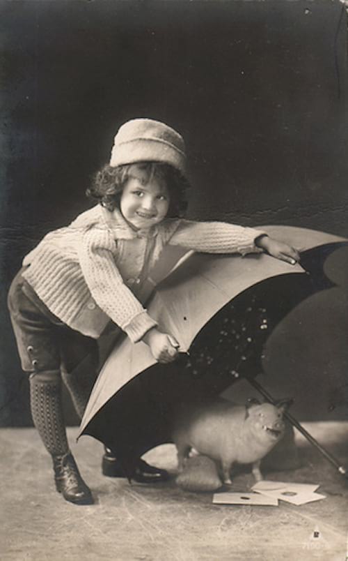 Väike tüdruk, kes hoiab maas vihmavarju, vihmavarju all on väike põrsas