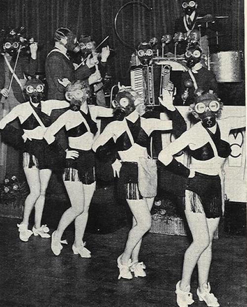 Varias mujeres en un escenario vestidas desnudas con una máscara y músicos detrás de ellas
