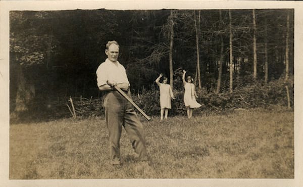 Vyras ant žolės su paslaptingu daiktu ant rankos ir dvi jaunos merginos, mojuojančios už jo