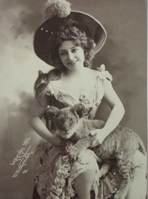 Mujer sentada en una silla equipada con un sombrero sosteniendo un cachorro de león en sus brazos