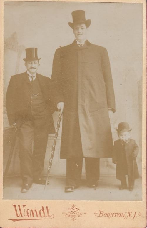 Du juodai apsirengę vyrai su didelėmis skrybėlėmis ir mažas berniukas šalia