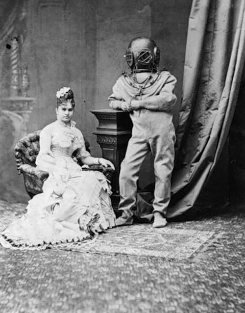 Mujer sentada con un vestido largo junto a una persona con un traje submarino