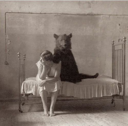 Mujer sentada en una cama y un oso de peluche junto a ella