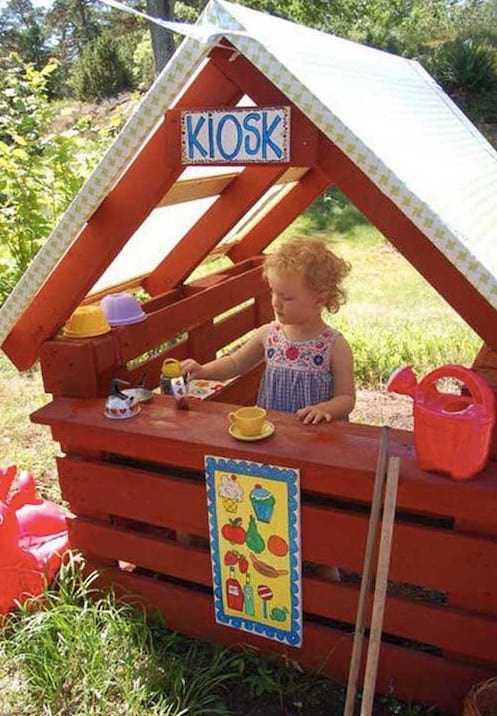 una botiga de queviures vermella feta amb un palet amb una nena jugant-hi