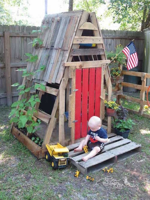 una bonica cabana amb una porta de palet vermella amb un nen jugant al davant