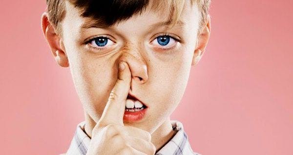 ילד צעיר עם עיניים כחולות תוקע את האצבע המורה שלו באפו.