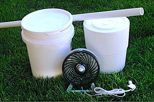 Un balde de albañil, un balde de poliestireno, un tubo de PVC y un ventilador de mesa para el aire acondicionado del hogar.