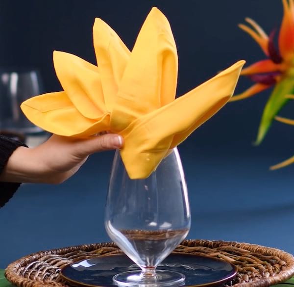 Servilleta amarilla doblada en forma de ave del paraíso en un vaso