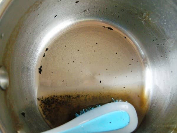 la sartén quemada se limpia con un cepillo de cocina después de remojar durante 6 horas