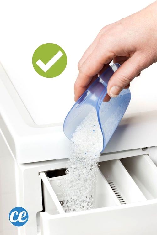 Una mano vertiendo detergente en polvo en el cajón de detergente de una lavadora.