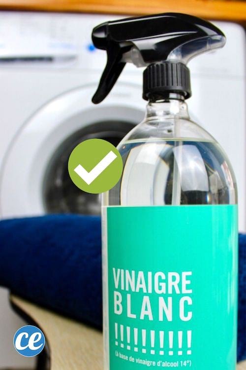 Una botella de spray de vinagre blanco delante de una toalla azul y una lavadora.