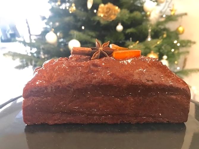 pan de jengibre con trozo de naranja y canela delante de un árbol de Navidad