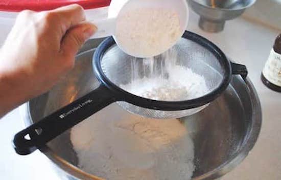 Primer paso de la receta fácil de panqueques caseros, pasar la harina y el polvo de hornear por un colador.