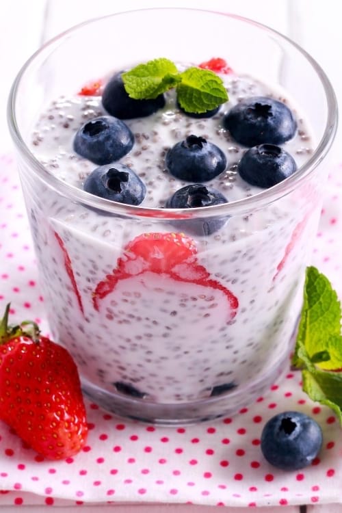 Un ramekin de vidrio con yogur, semillas de chía y fruta fresca, sobre un mantel de lunares rojos.