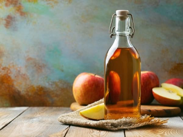 Una botella de vinagre de sidra de manzana con manzanas para ayudar a perder peso