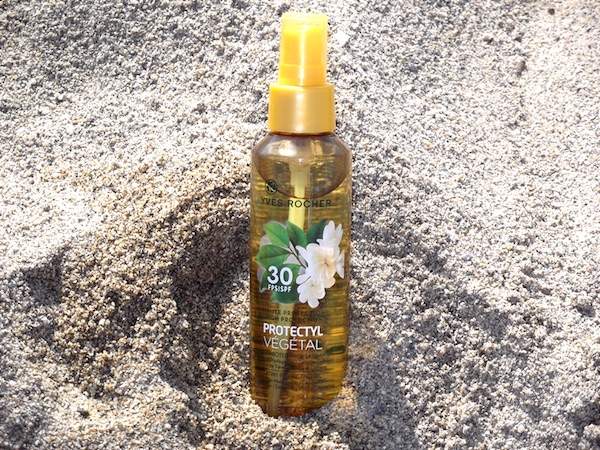 Una botella de spray de aceite solar Yves Rocher en la arena