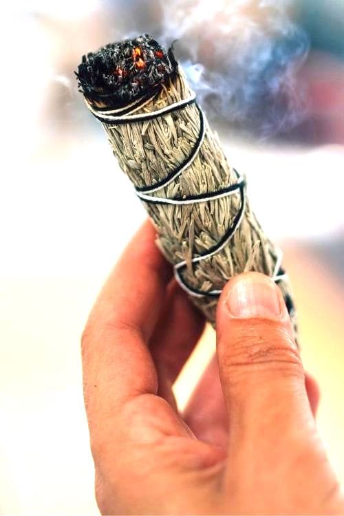 Una mano que sostiene una barra de salvia blanca que produce humo.