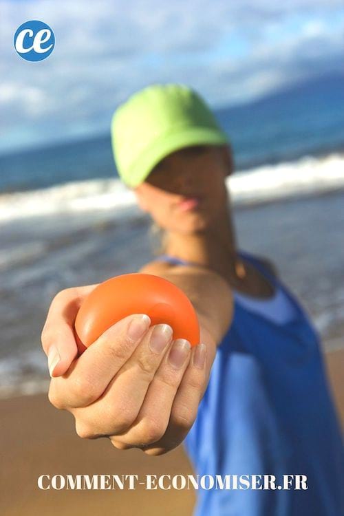 Uma mulher segurando um balel anti-stress vermelho na mão na praia.